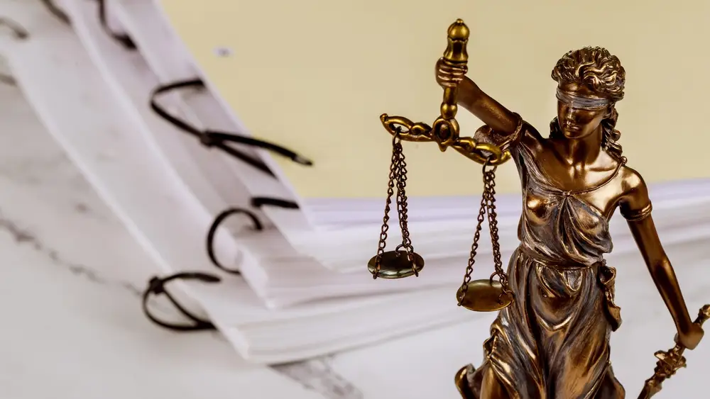 Eine Justitia-Figur neben zwei gebundenen Stapeln von Unterlagen
